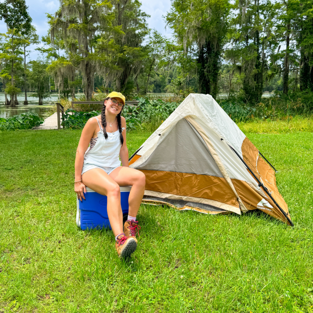 Happy camper sitting on cooler in front of tent at campsite at Florida Caverns RV Resort
